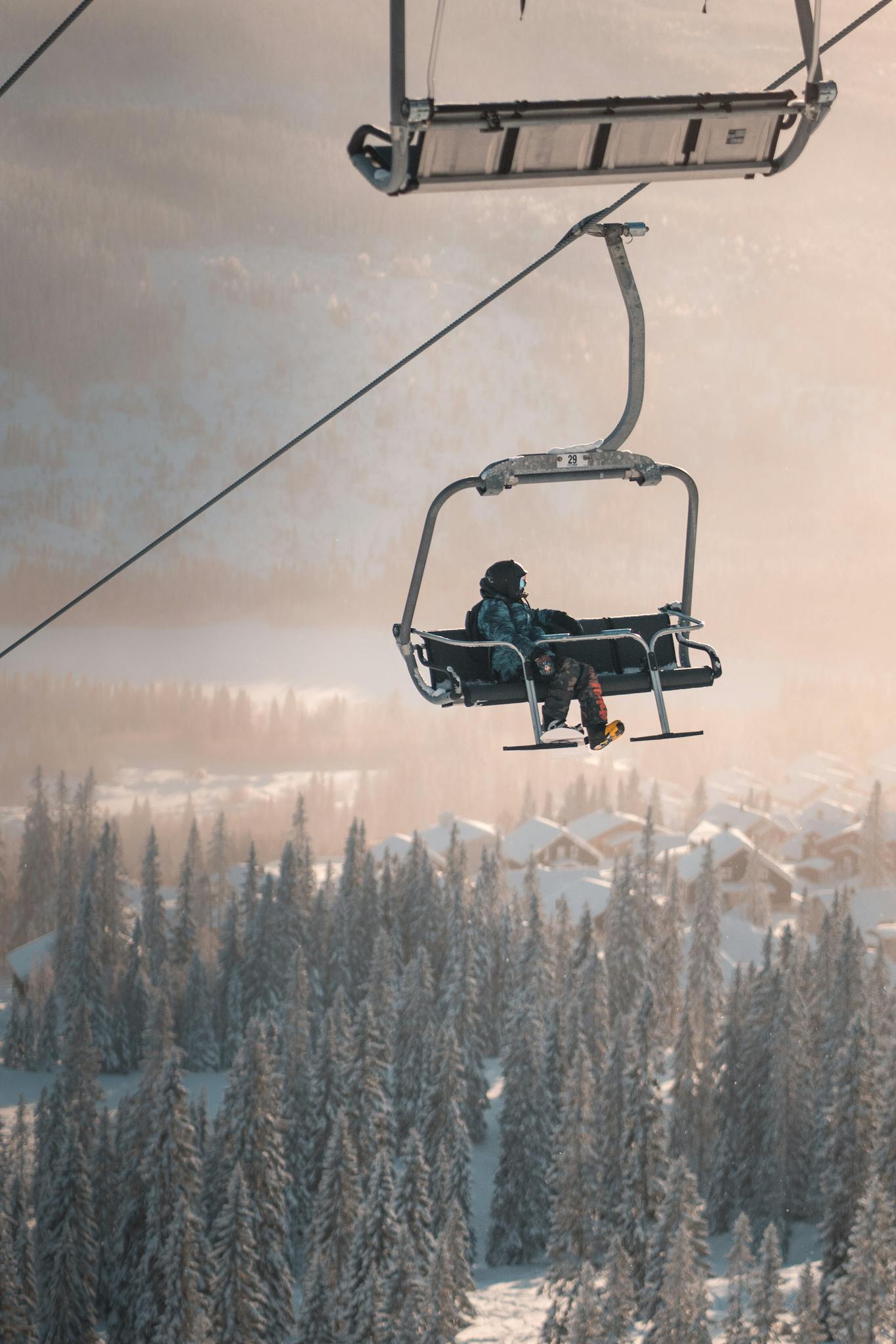 Ski lift carrying a snowboarder over a snowy forest in Åre, Sweden during winter.